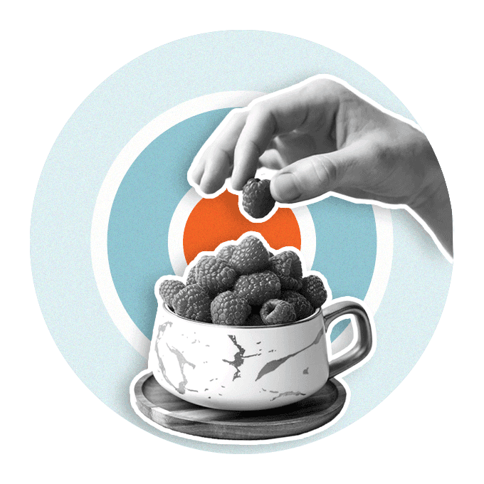 Person holding a berry above a cup full of berries sitting on a coaster, with target behind the image