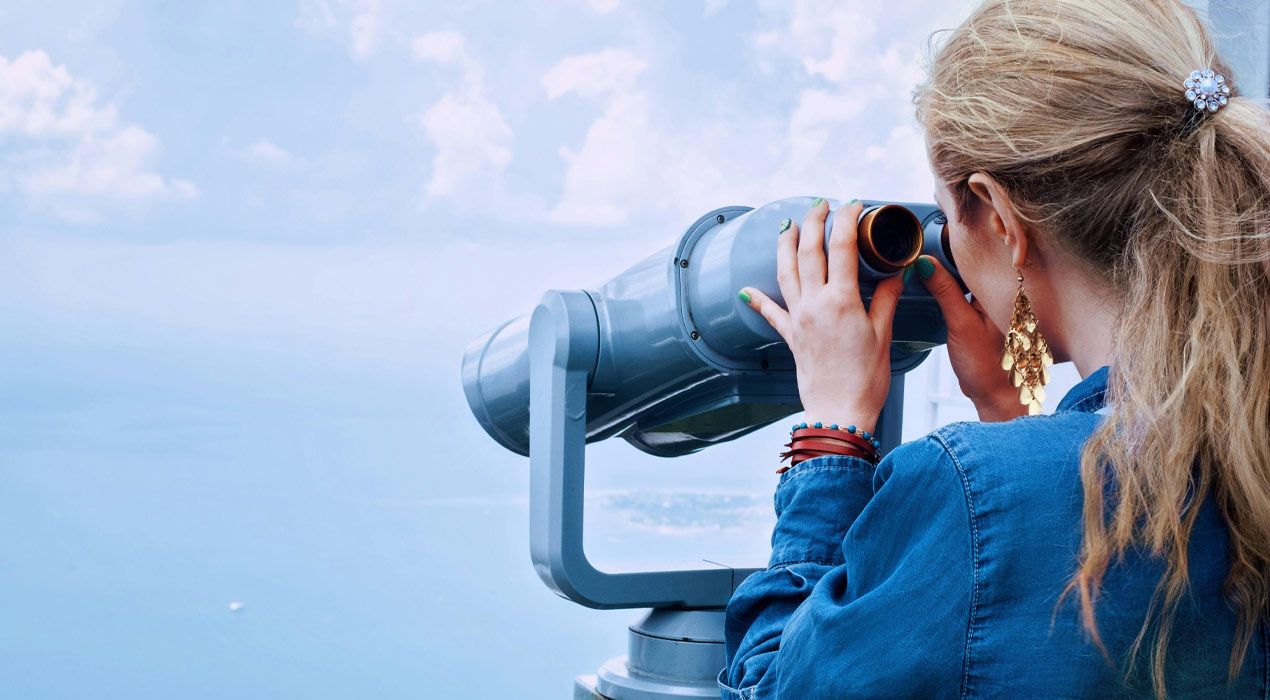 Young blonde woman looking out over the ocean through a pair of binoculars