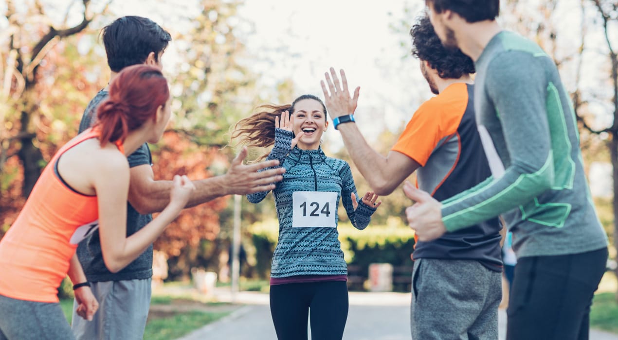 Jogger running across the finish line of a race, with people standing either side of her cheering her on