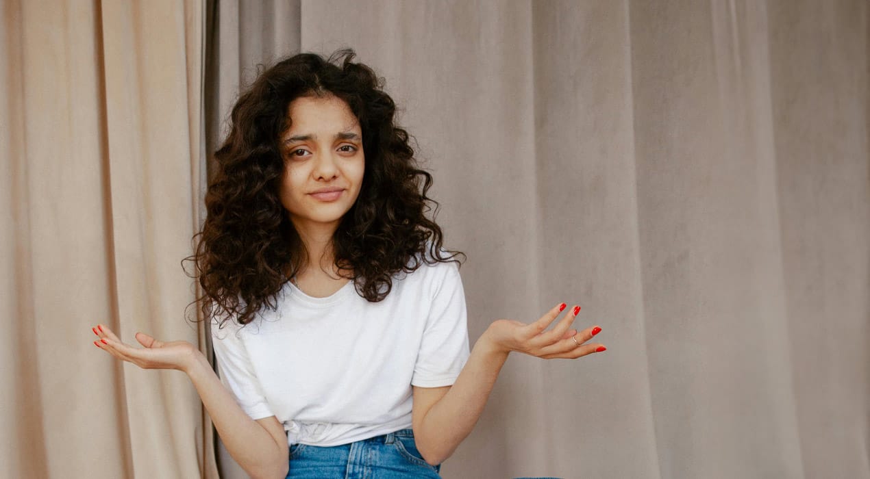 Young woman wearing jeans and a white t-shirt holding her arms up either side shrugging