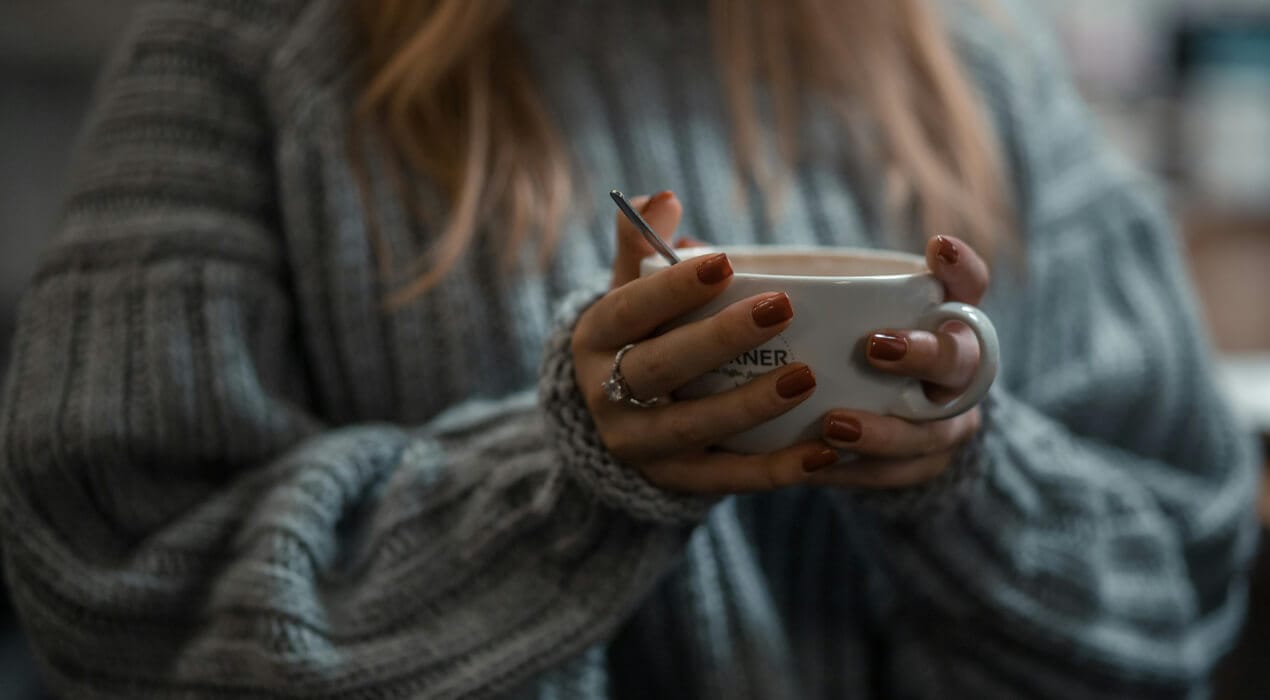 Close up of woman wearing a cosy sweater and holding a cup of tea