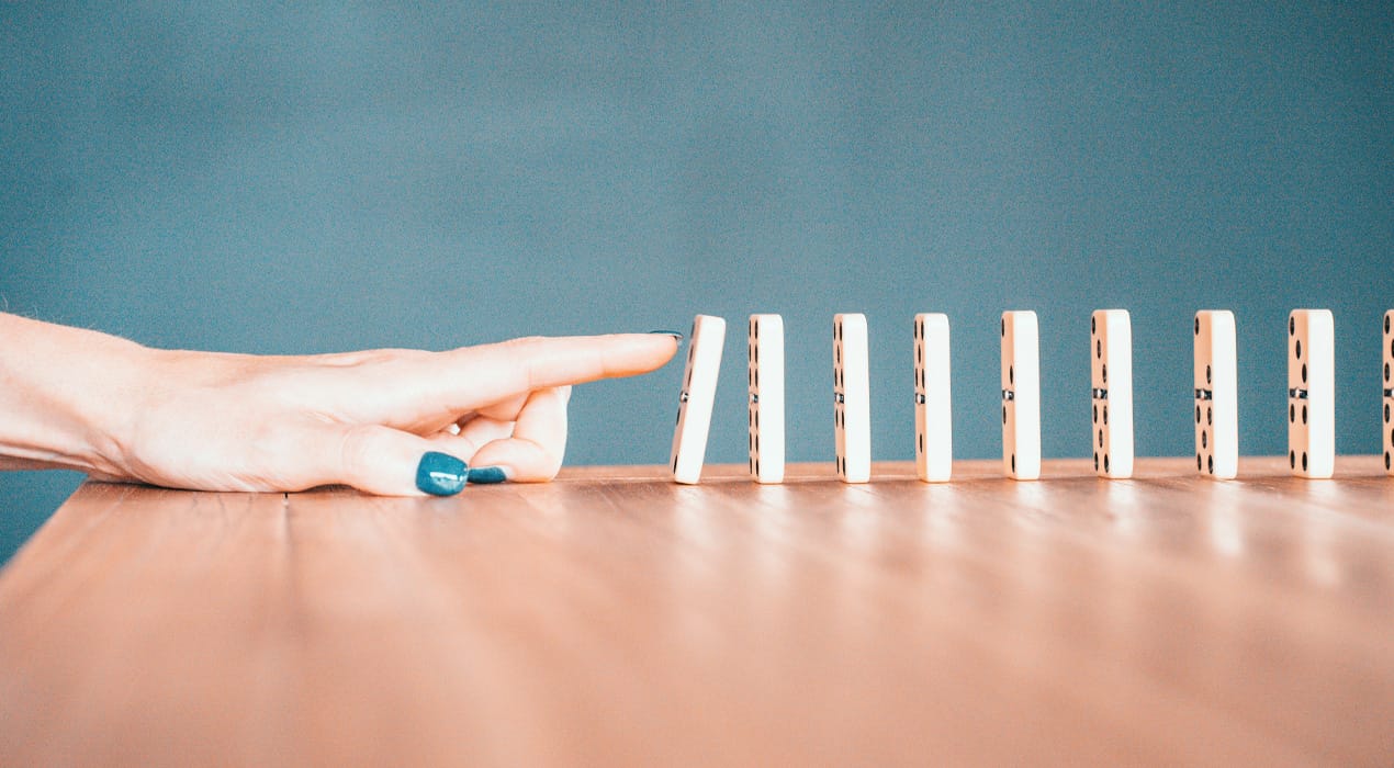 Hand pushing over the first in a line-up of dominoes on a table