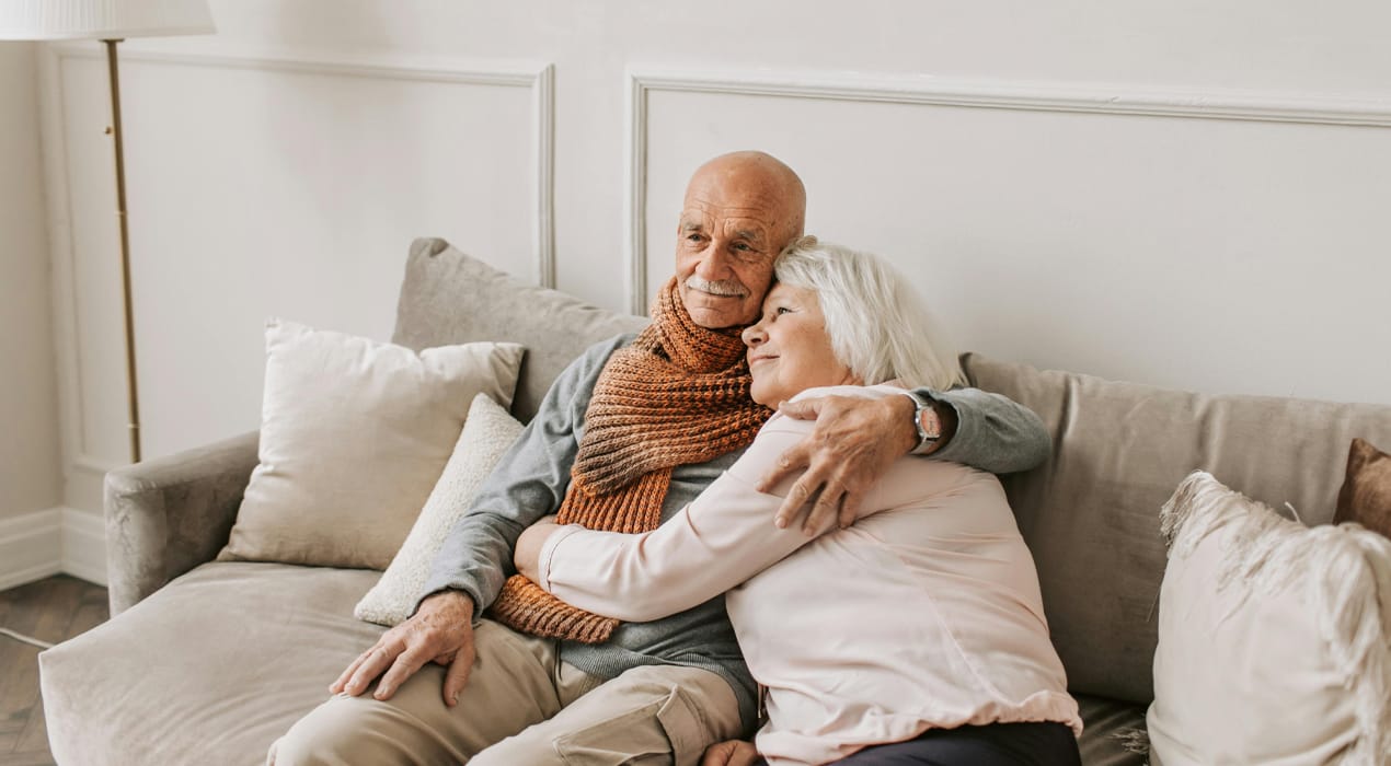 An older man and woman sitting on a couch, hugging.