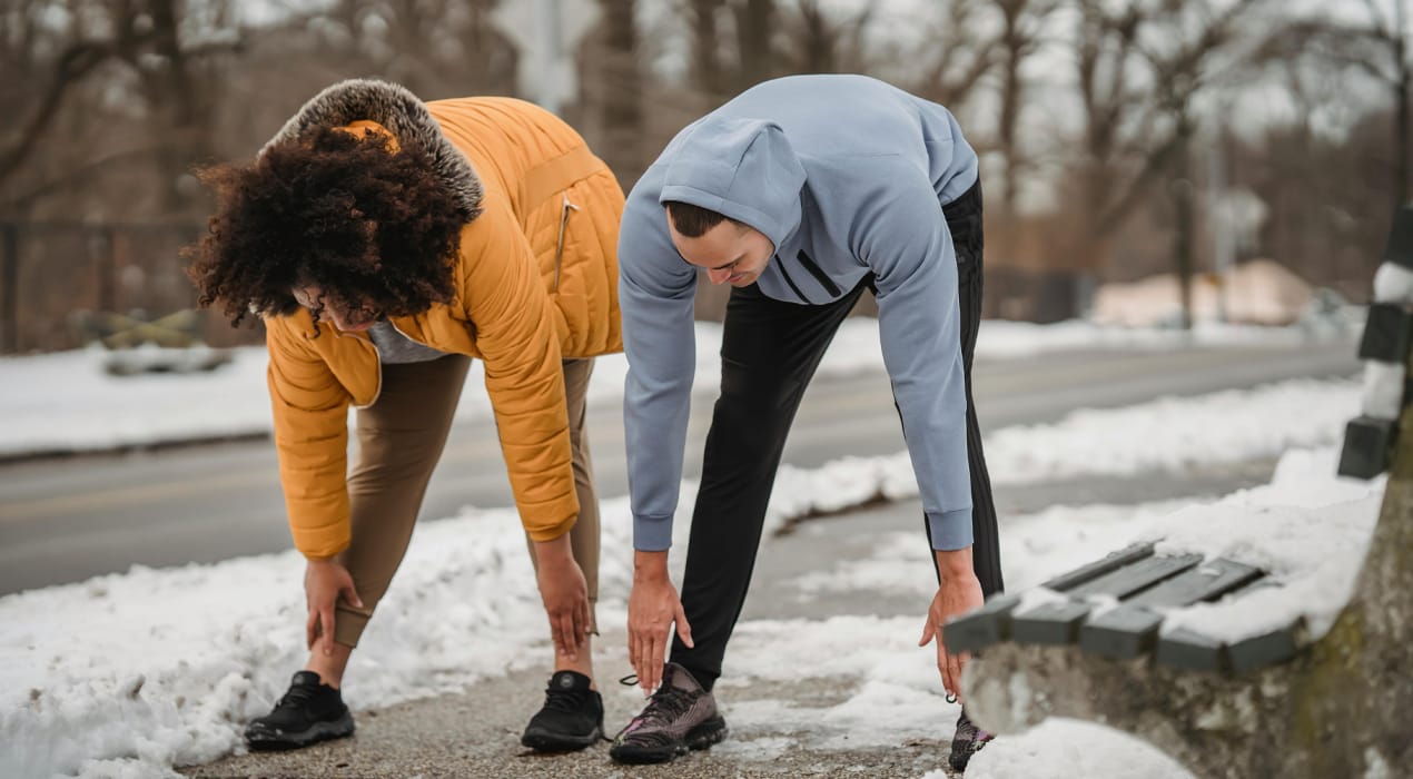 Two people stretching outside in winter with snow on the ground around them